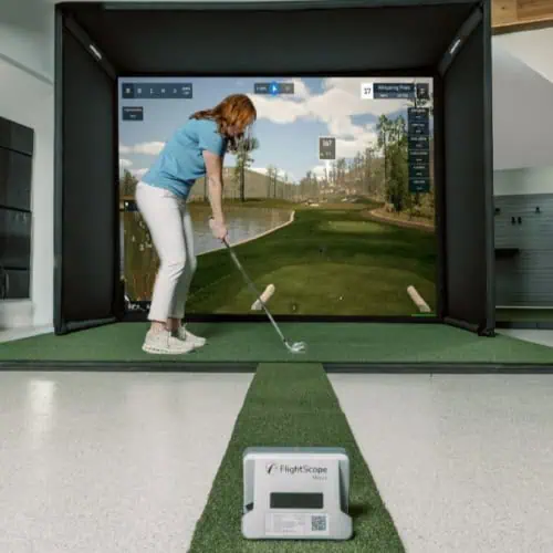 High-tech golf simulator setup with a woman practicing her swing indoors, showcasing advanced golf simulation technology and realistic outdoor golf course graphics.